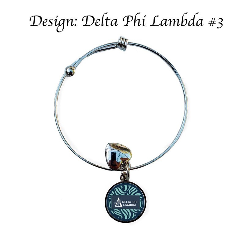 K&ouml;nnte beinhalten: Ein silbernes, ausziehbares Armband mit einem Anh&auml;nger, der ein blaues und gr&uuml;nes Wirbelmuster mit einem wei&szlig;en Dreieck und dem Text "Delta Phi Lambda" zeigt.