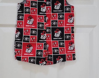 May include: A sleeveless jumper featuring a repeating grid pattern of red and black squares. Each square displays the University of Georgia bulldog mascot logo or the letter G. The garment has two black buttons at the shoulders and a white hanger.