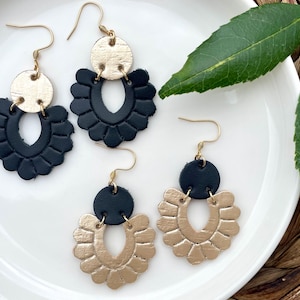 May include: A pair of dangle earrings with black and gold leather. The earrings feature a scalloped design and a round disc.