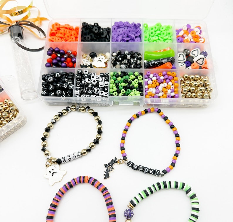 May include: A clear plastic storage box filled with various Halloween-themed beads, charms, and letters. The box includes black, white, green, purple, orange, and gold beads, as well as ghost, bat, and heart charms. The letters spell out "BOO" and "SPOOKY".