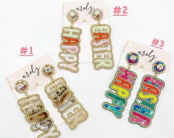 May include: Three pairs of colourful beaded earrings with the word "Happy" spelled out in sequins. The earrings are on white cards with the word "arely" written on them. The cards are numbered 1, 2, and 3.