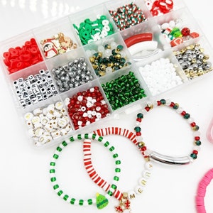 May include: A clear plastic storage box filled with various beads, charms, and letters for making Christmas bracelets. The box includes red and white striped beads, green and white beads, silver beads, red and white letter beads, and small Christmas-themed charms. Three bracelets are shown in the foreground, one with red and white striped beads, one with green and white beads, and one with silver beads and a charm.