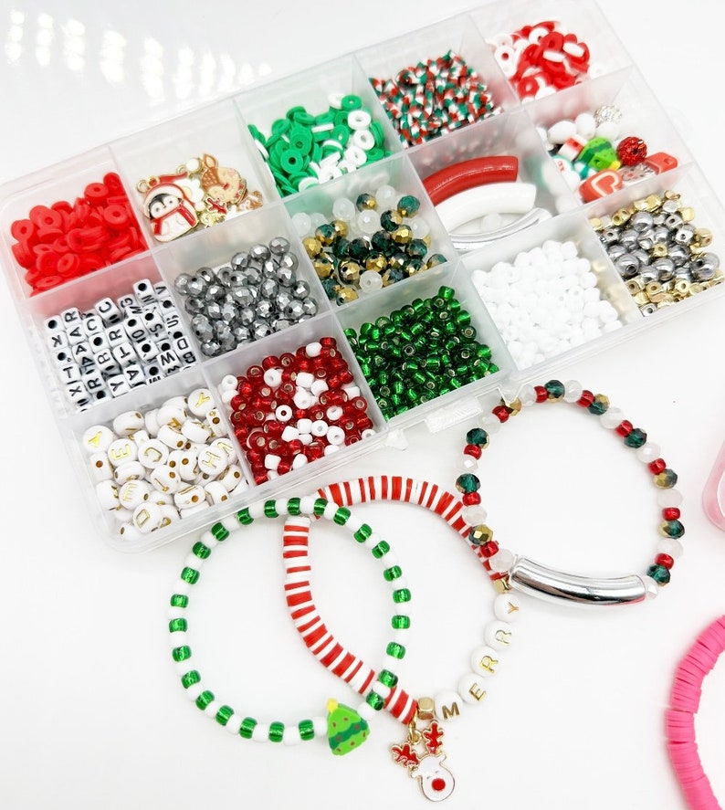 May include: A clear plastic storage box filled with various beads, charms, and letters for making Christmas bracelets. The box includes red and white striped beads, green and white beads, silver beads, red and white letter beads, and small Christmas-themed charms. Three bracelets are shown in the foreground, one with red and white striped beads, one with green and white beads, and one with silver beads and a charm.