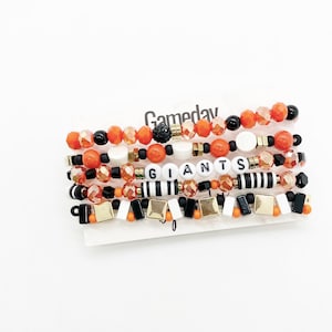 May include: A set of six bracelets featuring orange, black and gold beads. The bracelets spell out "GIANTS" in white letters. The bracelets are labelled "Gameday".