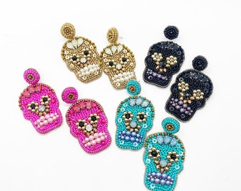 May include: Six pairs of beaded skull earrings in various colors, including gold, black, pink, and turquoise. The earrings are made with small beads and feature a skull design with intricate details.
