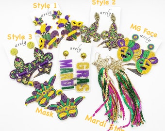 Peut inclure: Assortiment de boucles d'oreilles sur le thème du Mardi Gras avec différents motifs, notamment des fleurs de lys, des masques et des étoiles. Les boucles d'oreilles sont faites de perles de couleur verte, violette et dorée. Les textes "Mardi Gras" et "MG Face" sont visibles sur les cartes.