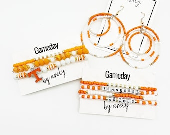 May include: Orange and white beaded bracelets with a charm that says "T" and the words "Gameday by arely". Another set of bracelets has the words "Tennessee Go Vols" in white beads.
