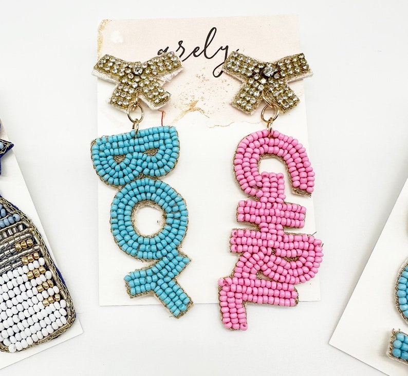 May include: A pair of beaded earrings with gold bows. One earring says "BOY" in blue beads and the other says "GIRL" in pink beads.