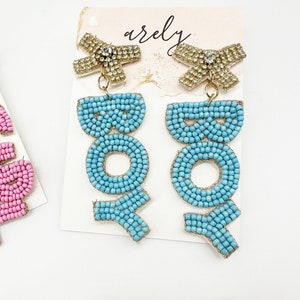 May include: A pair of blue beaded earrings with gold accents and a rhinestone bow. The earrings spell out the word "BOHO".