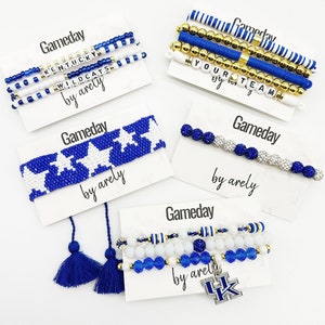 Puede incluir: Un conjunto de cuatro pulseras de cuentas azules y blancas con las palabras "Gameday", "Kentucky Wildcats", "Your Team" y "by arely". Las pulseras están en tarjetas blancas con las palabras "Gameday" y "by arely" escritas en ellas.
