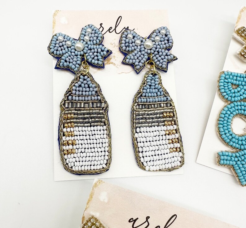 May include: A pair of blue and white beaded earrings with a baby bottle charm and a blue bow with a pearl accent.