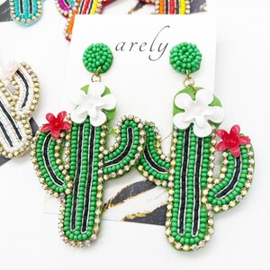 May include: A pair of green cactus-shaped earrings with white and red flowers. The earrings are made of beads and rhinestones.