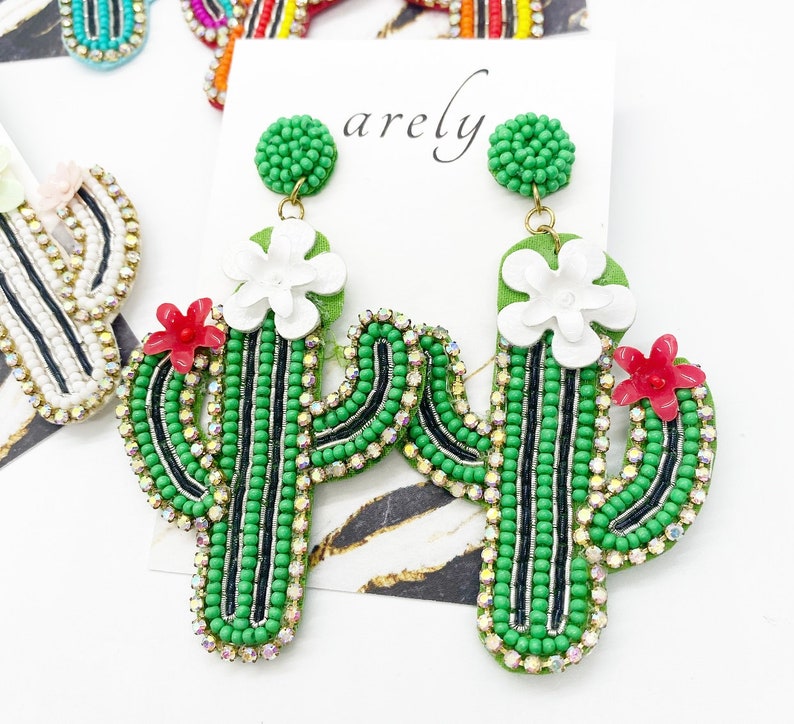 May include: A pair of green cactus-shaped earrings with white and red flowers. The earrings are made of beads and rhinestones.