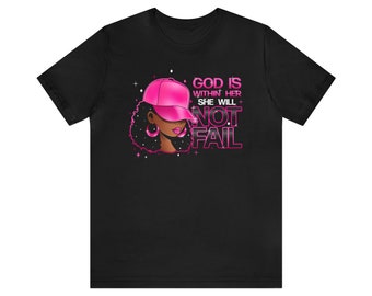 May include: Black t-shirt with a pink illustration of a woman wearing a pink baseball cap. The text "God is within her, she will not fail" is written in pink letters.