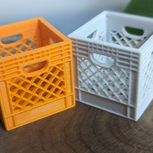 Puede incluir: Dos miniaturas de cajas de leche, una naranja y otra blanca. Las cajas son de plástico y tienen un patrón de rejilla.