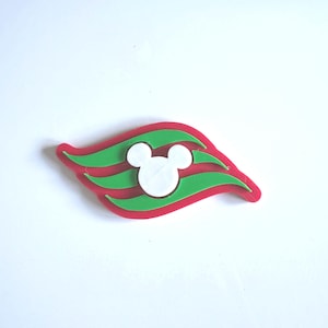May include: A decorative emblem featuring a red, wave-like base with two horizontal green stripes layered across the center. A white, circular silhouette of a mouse head with two rounded ears is positioned prominently in the middle of the design.