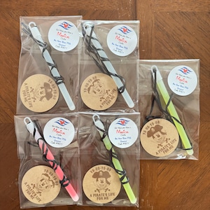May include: Five individual clear plastic bags each containing a glow stick with a black cord and a round tan wooden tag. The tags feature a pirate-themed Mickey Mouse illustration with the text "YO-HO-YO-HO A PIRATE'S LIFE FOR ME".