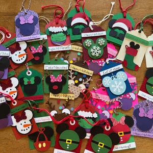 May include: A collection of colorful paper gift tags featuring various holiday-themed character silhouettes, including snowmen, stockings, and festive icons. Each tag includes a string loop and printed text such as Happy Holidays and Sparkle and Shine.