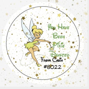 May include: A circular sticker featuring a cartoon fairy with blonde hair and a green dress, holding a wand. The background is white with gold star confetti. The text reads: You Have Been Pixie Dusted From Cabin #8022 in green and black.