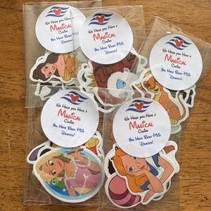 May include: Five clear plastic bags containing assorted Disney character stickers. Each bag features a circular white label with a red cruise ship icon and the text: We Hope you Have a MAGICAL Cruise You Have Been Pixie Dusted! Characters include Rapunzel, Alice, and Simba.