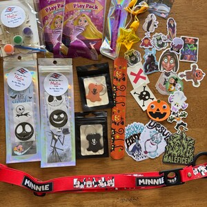 May include: A collection of Disney-themed items including two Rapunzel play packs, a purple pen, a yellow star charm, a red Minnie Mouse lanyard, two Jack Skellington sticker packs, two Mickey-shaped keychains, a pumpkin slap bracelet, and various character stickers.