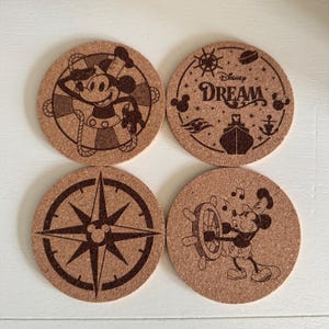 May include: Set of four round cork coasters with Disney-themed designs. One coaster features Mickey Mouse in a sailor outfit, another has the word "Dream" and a ship, a third has a compass, and the last shows Mickey at a ship's wheel.