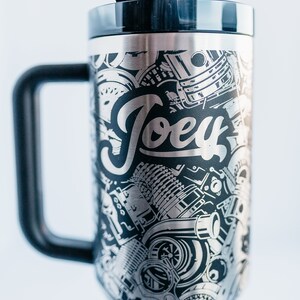 May include: Stainless steel travel mug with a black handle and lid. The mug features a detailed engraved design of engine parts and the name "Joey" in a stylized font. Includes a black straw.