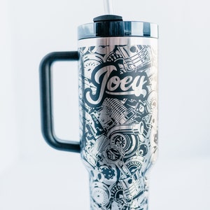 May include: Stainless steel tumbler with a black handle and lid. The tumbler is covered in a detailed silver and black design of engine parts and the name "Joey". Includes a clear straw.