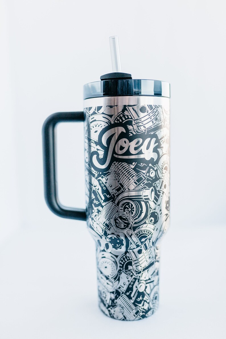 May include: Stainless steel tumbler with a black handle and lid. The tumbler is covered in a detailed silver and black design of engine parts and the name "Joey". Includes a clear straw.
