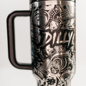May include: Stainless steel travel mug with a black handle and lid. The mug is covered in a detailed, etched design of engine parts and the word "DILLY" in a bold font. The mug is designed to keep beverages hot or cold.