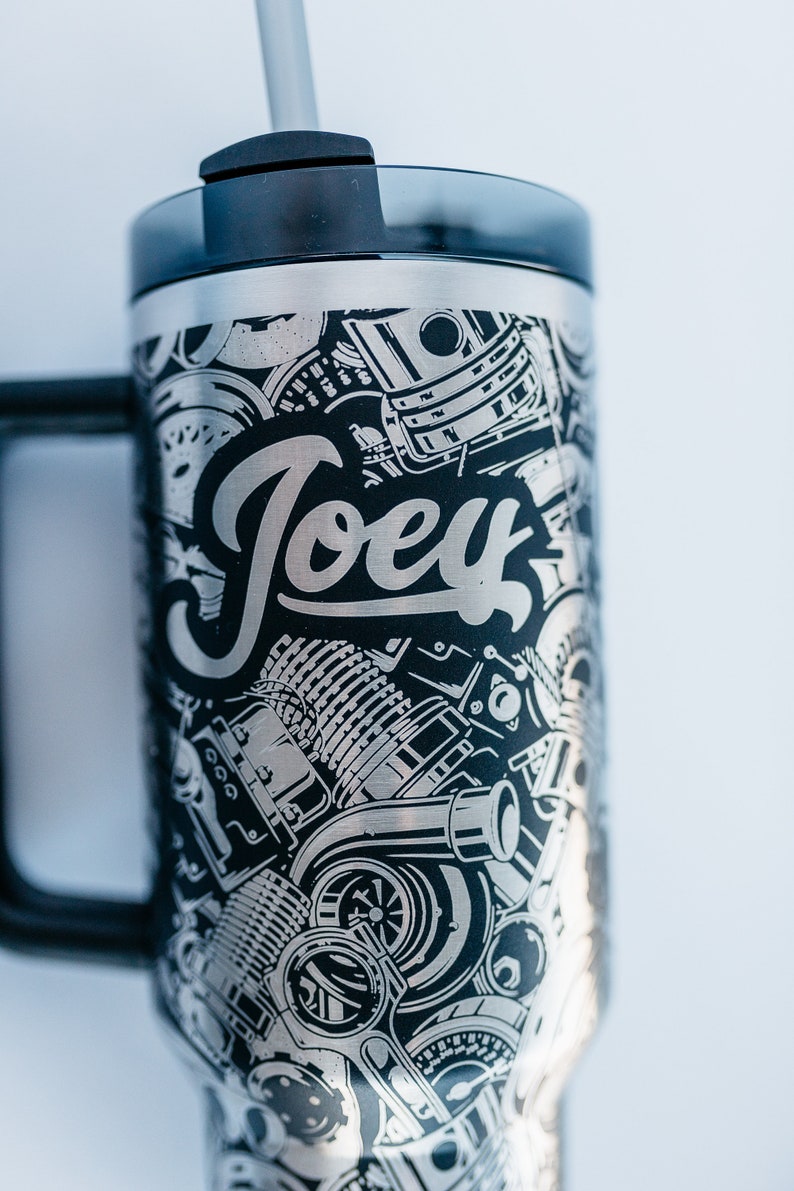 May include: Stainless steel tumbler with a black handle and lid. The tumbler features a detailed graphic design of engine parts and the name "Joey" in a stylized font. Includes a gray straw.