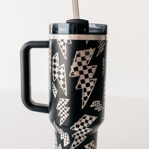 Op de afbeelding: Zwarte ge&iuml;soleerde beker met een handvat en een deksel, met een zilveren rietje. De beker is versierd met een patroon van bliksemschichten gevuld met een dambordontwerp. De handgreep en het deksel zijn zwart.