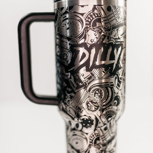 May include: Stainless steel travel mug with a black handle and lid. The mug is covered in a detailed black and silver design of engine parts and the word "DILLY".