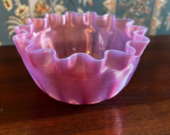May include: A pink glass bowl with a ruffled edge and a ribbed pattern. The bowl is made of clear glass with a pink tint.