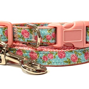 May include: A pink and blue floral dog collar and leash set. The collar has a pink plastic buckle and the leash has a silver hook.
