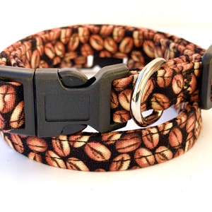 May include: A brown and black dog collar with a coffee bean pattern. The collar has a black plastic buckle and a silver metal D-ring.