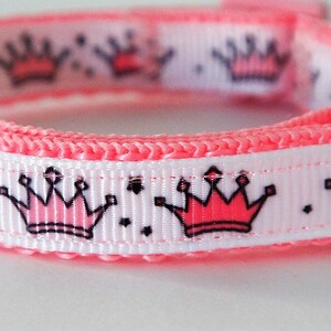 May include: Pink and white dog collar with a repeating pattern of pink crowns with black outlines.