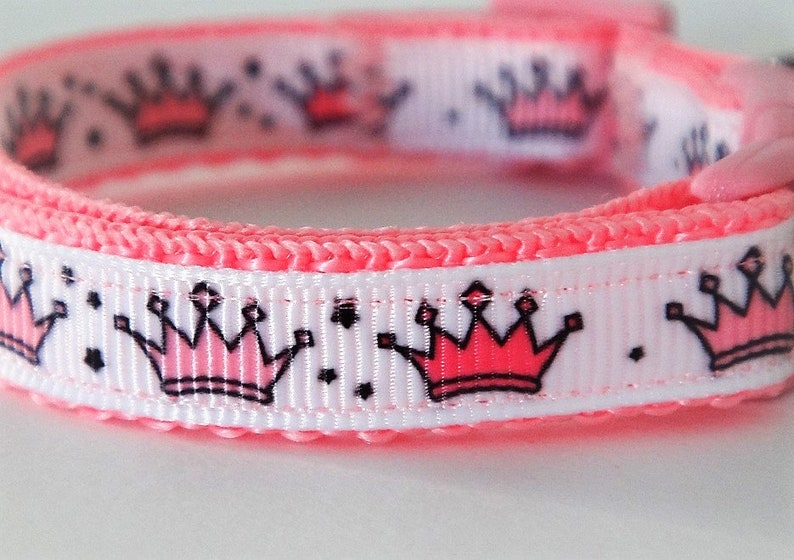 May include: Pink and white dog collar with a repeating pattern of pink crowns with black outlines.