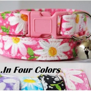 May include: Pink cat collar with a white daisy print and a pink buckle. The collar has a bell attached to it. The text "...In Four Colors" is visible below the collar.