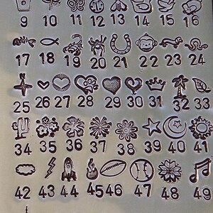 May include: A metal sheet with various small, engraved designs and corresponding numbers. The designs include paw prints, a bone, a cat, a skull, a coffee cup, a dragonfly, a butterfly, a bee, a duck, and more.