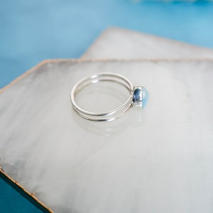 May include: A silver ring with a light blue oval gemstone. The ring is on a white background.