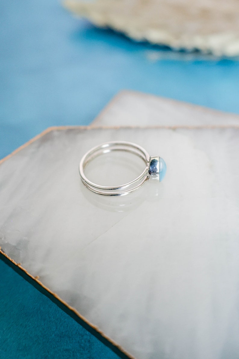 May include: A silver ring with a light blue oval gemstone. The ring is on a white background.
