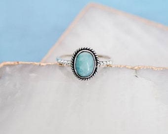May include: A silver ring with a light blue oval gemstone set in a rope-like border.