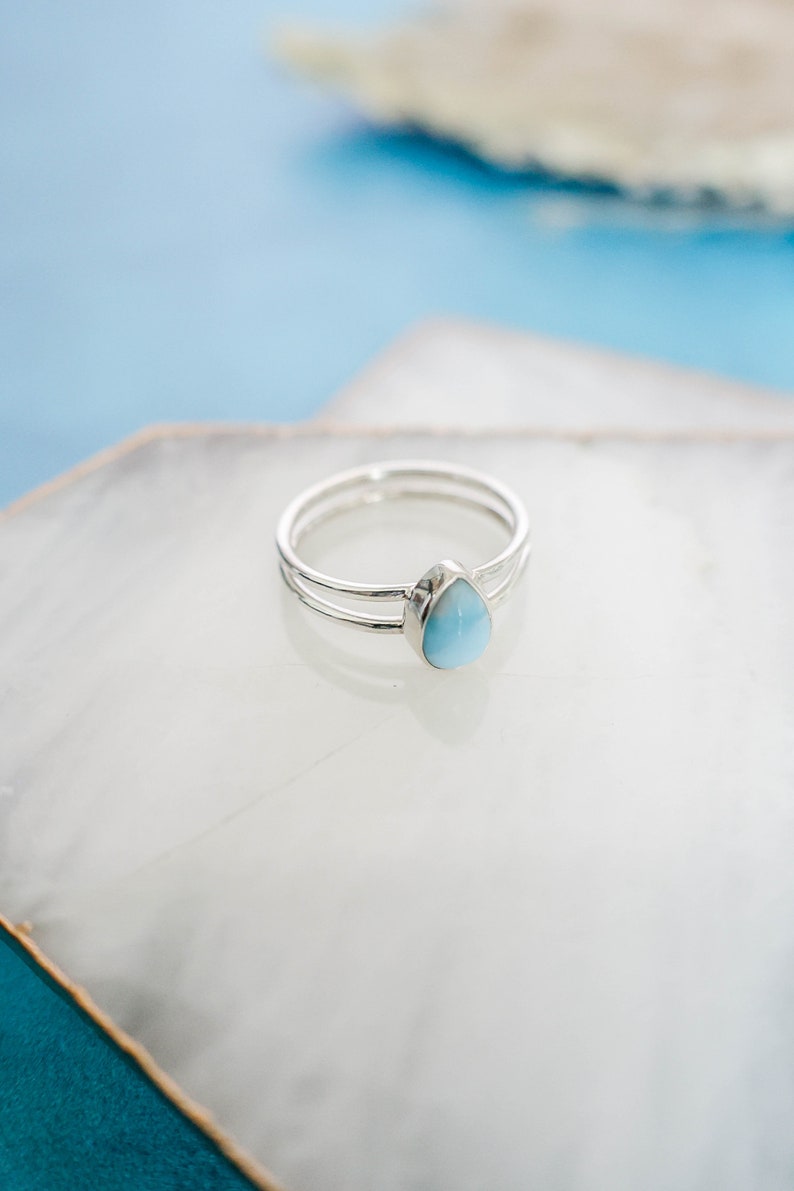 May include: A silver ring with a teardrop-shaped blue gemstone.