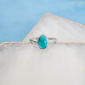 May include: A silver ring with a teardrop-shaped turquoise stone.