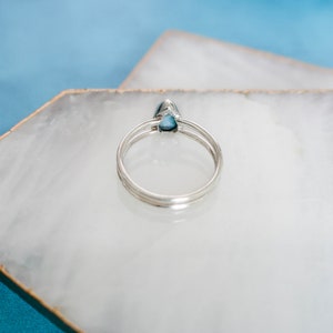 May include: A silver ring with a teardrop-shaped blue gemstone. The ring is on a white marble surface.