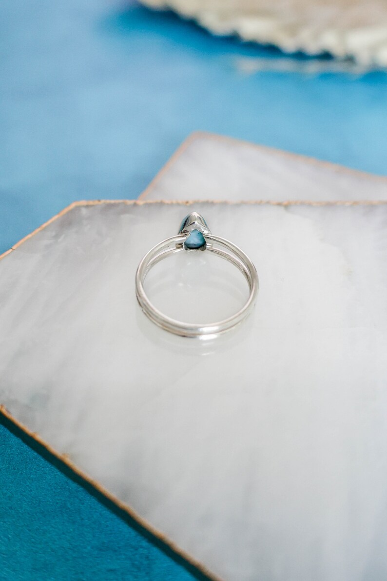 May include: A silver ring with a teardrop-shaped blue gemstone. The ring is on a white marble surface.