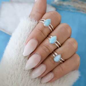 May include: Three silver rings with teardrop-shaped turquoise gemstones. The rings are stacked on a finger with light pink nail polish.