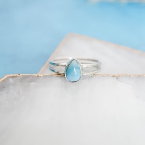May include: A silver ring with a teardrop-shaped blue gemstone. The ring has a double band.