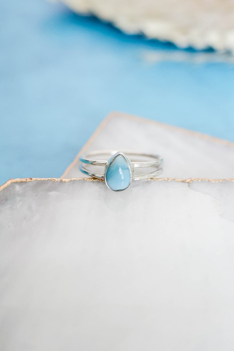 May include: A silver ring with a teardrop-shaped blue gemstone. The ring has a double band.